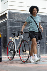 African-American man walking white bike red rim on sidewalk wearing black crossbody bag, copy space © wavebreak3