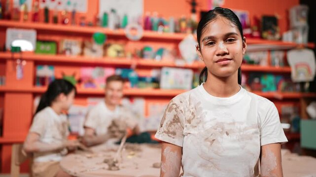 Smiling student looking at camera while diverse student having workshop at art lesson. Caucasian girl smile while sitting and attend in pottery class with happy multicultural children. Edification