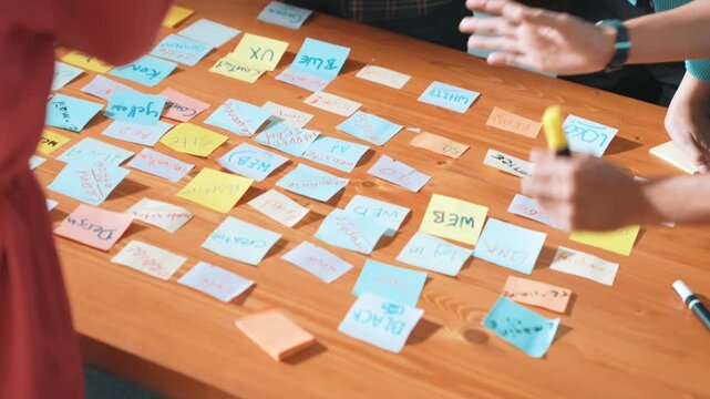 Top view of project manager sticking sticky notes and explain idea about web design. Professional marketing team or programmer brainstorming idea while looking at tablet with color palette. Symposium.