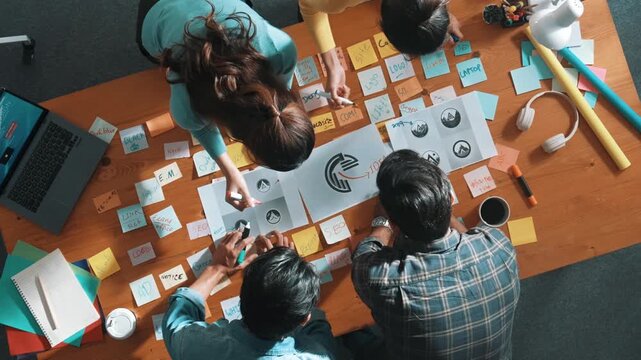 Top view of business team write graphic logo on meeting table with colorful sticky notes and design while explain idea. Project manager sharing idea and explain concept art to smart team. Symposium.