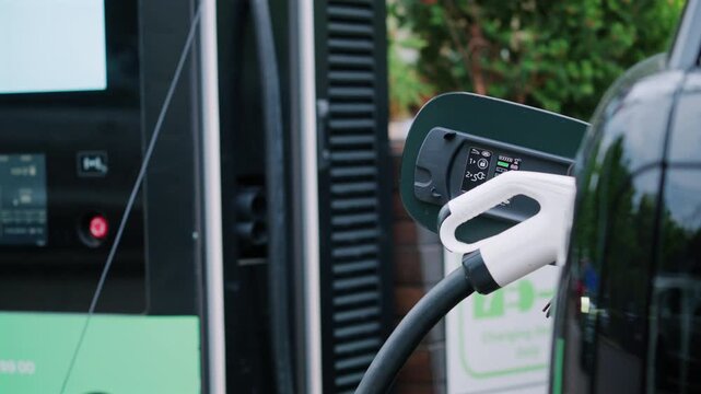 Electric vehicle charging at a modern station, with a close up of the connector plugged into the car