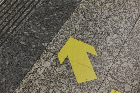 Yellow directional arrow painted on speckled granite floor indicating movement forward