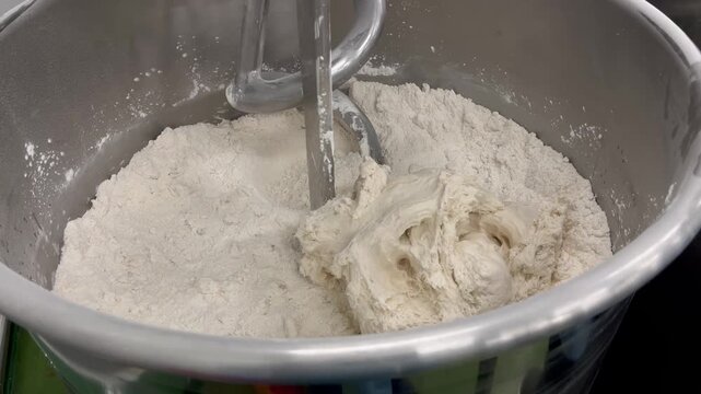 Dough being mixed and kneaded in an industrial mixer during food manufacturing operations. Continuous mixing process used to develop dough structure, improve consistency, and support large-scale baker