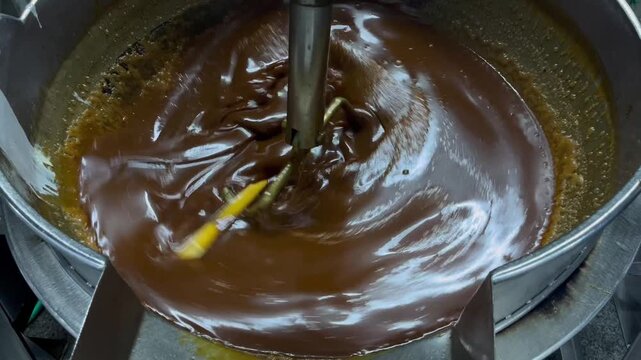 Caramel sauce being continuously mixed in an industrial steam-heated kettle during food manufacturing operations. Large-scale cooking process supporting product consistency, texture control, and comme