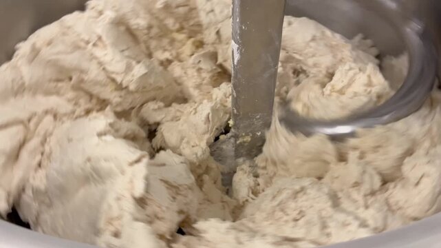 Dough being mixed and kneaded in an industrial mixer during food manufacturing operations. Continuous mixing process used to develop dough structure, improve consistency, and support large-scale baker