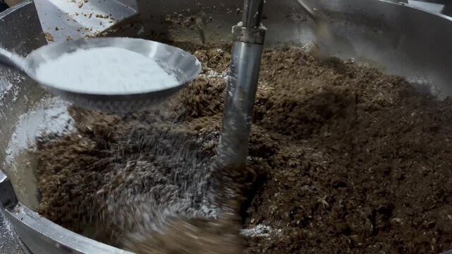 Worker adding dry ingredients into an industrial mixing kettle during food manufacturing operations. Ingredient incorporation process supporting recipe control, product consistency, and large-scale fo