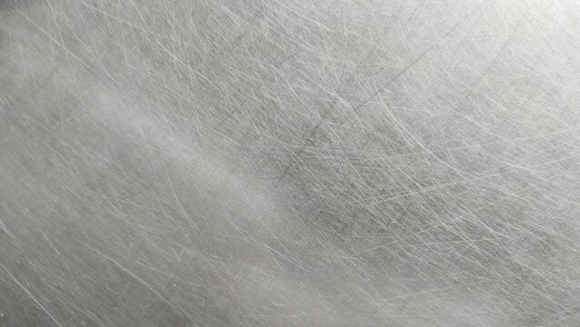 close-up of a scratched metal surface, possibly stainless steel or aluminum. The texture is rough, with numerous fine and deep scratches crisscrossing in various directions, creating a worn and aged