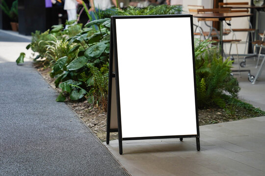 Blank white outdoor advertising stand sandwich board mock up template. Clear street signage board placed by an outdoor dinning area of a restaurant.