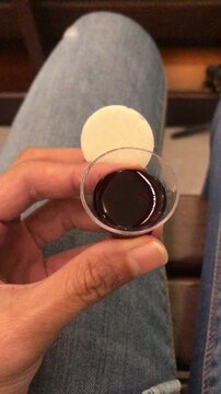 A person's hand holds a communion wafer and a small cup of dark liquid, likely wine, in preparation for a religious service.