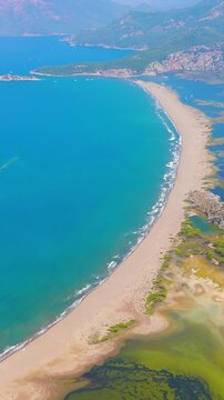 Vertical video. Dalyan, Turkey. Iztuzu Beach, a 4.5-kilometer sand spit separating the Dalyan River delta from the Mediterranean Sea, aerial view with mountain backdrop. Aerial View. Rich colors