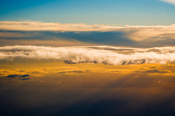 Fototapeta premium Bright evening sun rays pierce long fluffy cumulus cloud formations over the dark earth ground surface before the sunset time.