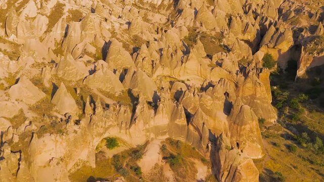 Goreme, Nevsehir, Turkey. Fairy chimney rock formations and eroded tuff pillars glowing in warm golden hour light, aerial panoramic view over the vast Cappadocia landscape. Aerial View, MasterShots, 