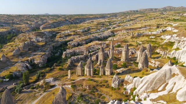 Goreme, Nevsehir, Turkey. Gorkundere Rocket Valley, towering phallic rock spires and fairy chimneys rising from golden terrain, aerial view under clear blue sky. Aerial View, MasterShots, Spiral forw