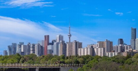 Naklejka premium A wide panoramic evening view of illuminated skyscrapers in the Toronto financial center rising above a dark treeline and highway in Ontario Canada