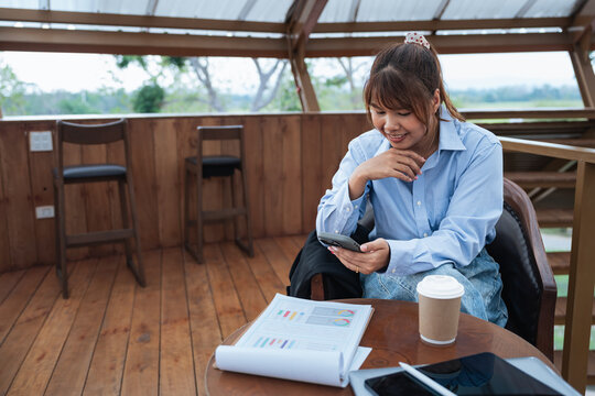 Woman is engaged in financial planning and discussion while reviewing data and analysis on documents and smartphone in cozy wooden room with natural light