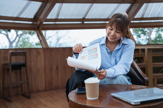 Young woman is engaged in financial planning and data analysis while reviewing charts and graphs during discussion in cozy wooden workspace with laptop and coffee cup nearby