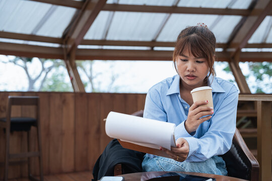 Young woman holding coffee cup and reviewing document with data analysis and financial planning discussion in casual indoor workspace environment