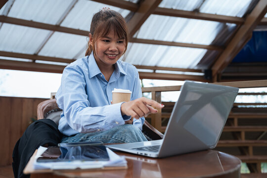 Young woman holding coffee cup pointing at laptop screen during financial planning discussion with data analysis on table in modern workspace