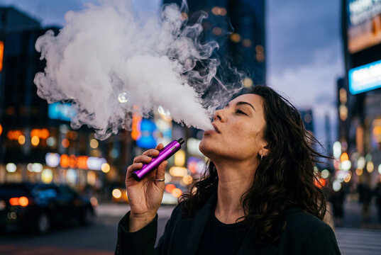 Woman smoking purple vape pen and blowing vapor cloud on city street