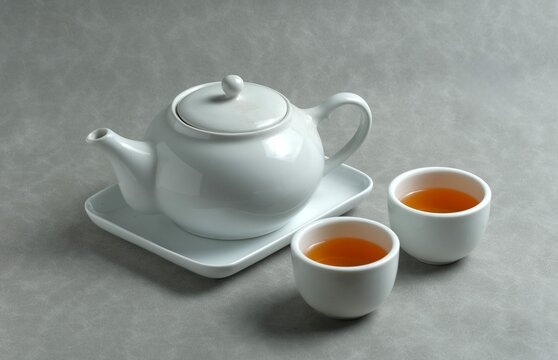 Minimalist white ceramic teapot and cup filled with warm tea on a clean background