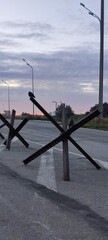 Black anti-tank obstacles (Czech hedgehogs) standing on an empty asphalt road under cloudy sky © Oleg