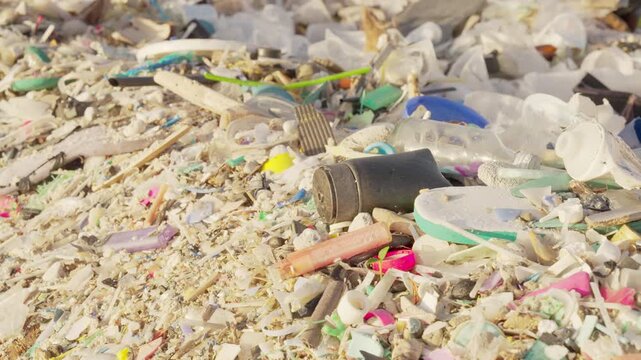 Panning shot of microplastics and plastic waste in sand on a beach, indonesia, southeast asia