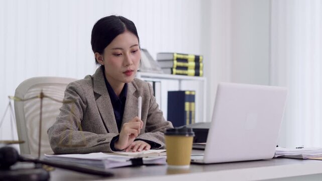Asian lawyer professional business woman review legal documents writing notes with laptop computer in modern law firm office workspace studying case files