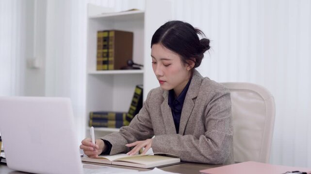 professional Asian lawyer businesswoman working with laptop computer notebook writing legal documents report at modern office desk concentrate focus study case