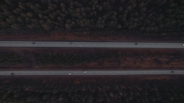 Top-down drone footage of a multi-lane highway cutting through dense autumn forest with moving cars, filmed in the Ural region, Russia, scenic travel transport view