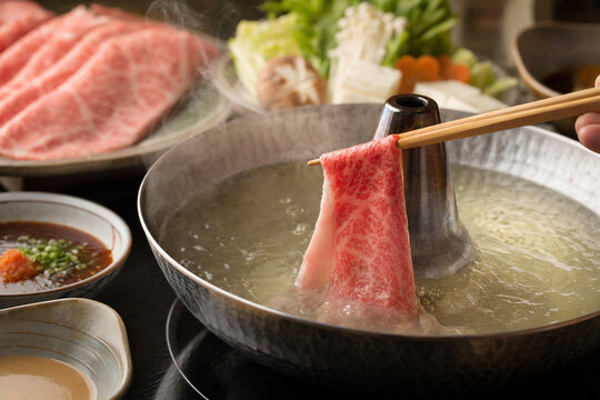 Close-up of Shabu-shabu, a thin slice of marbled wagyu beef being dipped into a simmering hot pot