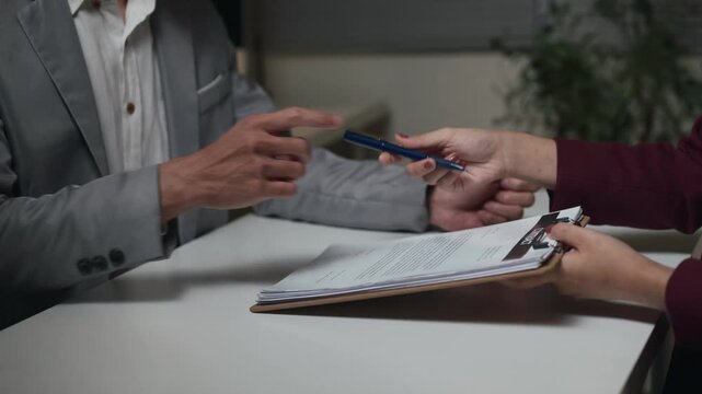 Business professionals discussing contract documents at office desk with pen and paperwork in formal meeting