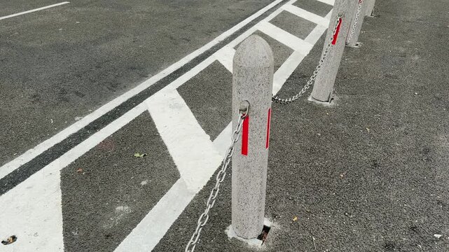 Concrete Bollards with Metal Chain and Road Markings on Asphalt