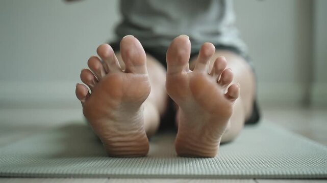 Individual performing yoga on a mat, focusing on foot positioning and alignment, showcasing toes and soles in a serene indoor environment with soft lighting