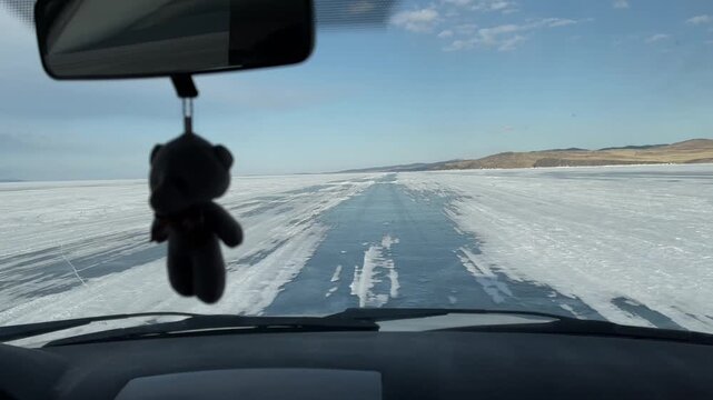 POV from inside a car driving along an ice road across frozen Lake Baikal in winter, with clear blue sky and distant hills, Siberia, Russia