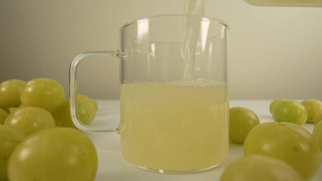 Fresh Indian gooseberry juice pouring into a glass cup from a bottle. Amla juice. Phyllanthus emblica.