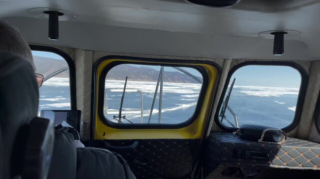 Interior view from a hovercraft cabin moving over cracked ice and snow on Lake Baikal in Siberia, Russia, with wide winter horizon seen through windows