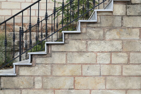 An outdoor staircase featuring modern white marble steps, situated in front of a rustic stone wall 