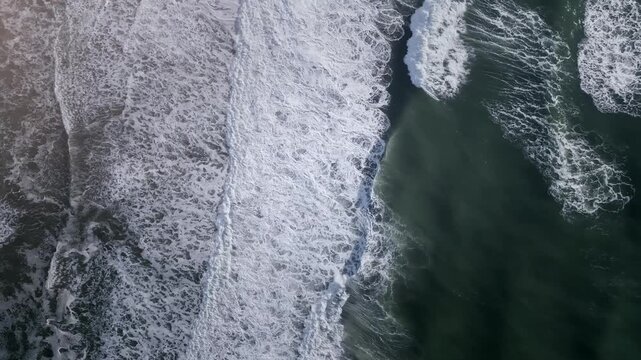 Top down aerial footage of rolling ocean waves creating white sea foam patterns over dark green water near the coast, natural seascape background with copy space
