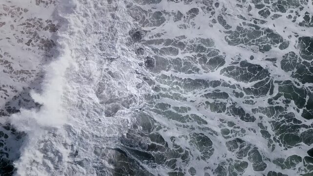 Top down aerial footage of turbulent ocean surface with white sea foam patterns and rolling waves, natural water background texture for coastal and marine themes