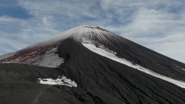 Wide shot of Avachinsky Volcano with dark volcanic slopes and remaining snowfields under dramatic clouds in Kamchatka Krai, Russia, remote wilderness landscape