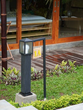House number sign 1A hanging on a modern outdoor garden lamp post near a wooden building facade during the daytime