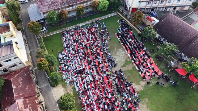 Aerial drone perspective captures large communal prayer on red mats, showcasing unity and spiritual atmosphere in open field.