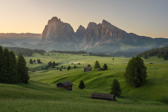 Beautiful sunrise view of Seiser Alm (Alpe di Siusi) with wooden huts, green meadows and dramatic Dolomite mountains in South Tyrol, Italy. Scenic landscape of European Alps in summer.