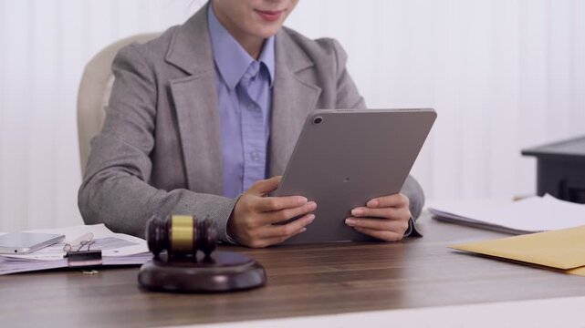 Asian lawyer businesswoman reviewing legal case documents using tablet computer in law office with gavel on desk professional attorney consultant study case
