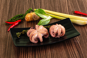 Grilled octopus on black plate surrounded by spices and ingredients © Andrei Starostin