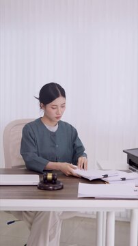 young Asian woman lawyer review legal document contract paper gavel desk prepare case judgment research legislation consultation attorney law firm office