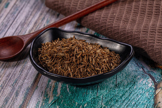 Dried cumin seeds in black bowl with wooden spoon