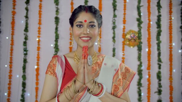 Bengali woman greeting in traditional Indian namaste while looking at the camera. Medium shot of an Indian female happily joining hands in namaste gesture on Durga Puja festival celebrated in India