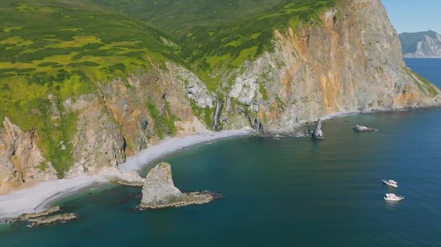 Drone footage of steep coastal cliffs, green tundra slopes and a secluded beach with rock stacks in Avacha Bay, Kamchatka Krai, Russia, summer seascape