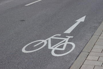 Obraz premium Bicycle lane marking on asphalt road with directional arrow indicating safe path for cyclists alongside cobblestone sidewalk in urban environment